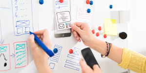 Collaborators writing on a whiteboard covered with magnets and sticky notes.